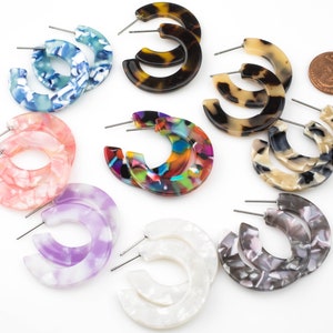 May include: Assortment of 10 pairs of colorful, patterned hoop earrings. The earrings are made of acrylic and have a marbled or tortoiseshell design. The earrings are approximately 2 inches in diameter.