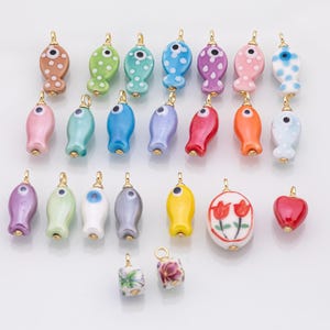 May include: A collection of colorful ceramic charms with gold-tone loops. The charms are fish-shaped, with various patterns and colors, including polka dots and floral designs. Other charms include a heart and a cube.