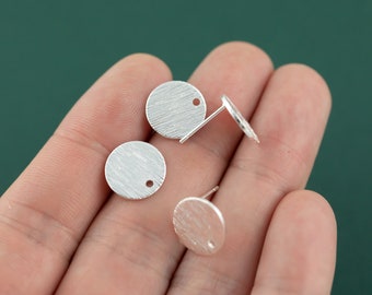 Puede incluir: Tres blancos de pendientes redondos de plata con una superficie texturizada y un pequeño agujero en el centro.