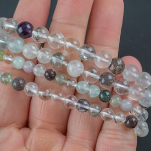 Könnte beinhalten: Ein mehrreihiges Armband aus klaren Quarzperlen mit Einschlüssen in verschiedenen Farben, darunter Grün, Braun und Lila.