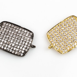May include: Two rectangular jewelry clasps, one in black and one in gold, both covered in small, clear rhinestones.
