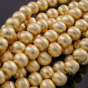 May include: A strand of gold-colored beads with a textured surface. The beads are round and have a metallic sheen.