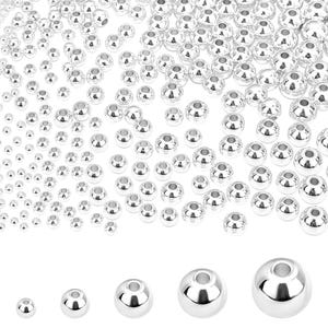 Puede incluir: Colección de cuentas plateadas brillantes de varios tamaños. Las cuentas son redondas con un agujero en el centro, adecuadas para la fabricación de joyas o manualidades. Las cuentas están dispersas sobre una superficie blanca.