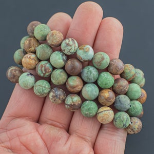 May include: A strand of green and brown agate beads, with a mottled pattern, in a hand.