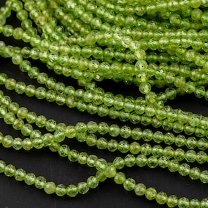May include: A strand of green peridot beads, faceted and round, with a shiny, translucent finish. The beads are strung on a clear thread and are arranged in a loose, flowing pattern.