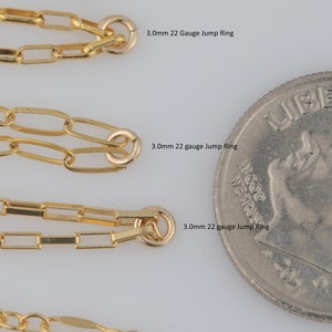 May include: Five gold jump rings of different sizes next to a US quarter. The jump rings are 2.8mm and 3.0mm in diameter. The text on the image reads "2.8mm 22 Gauge Jump Ring", "3.0mm 22 Gauge Jump Ring", "3.0mm 22 gauge Jump Ring", "3.0mm 22 gauge Jump Ring", and "3.0mm 22 gauge Jump Ring".