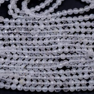 May include: Close-up of multiple strands of clear, faceted beads. The beads are small, round, and have a sparkling, crystalline appearance. The beads are strung together, creating a textured and layered effect. The background is dark.