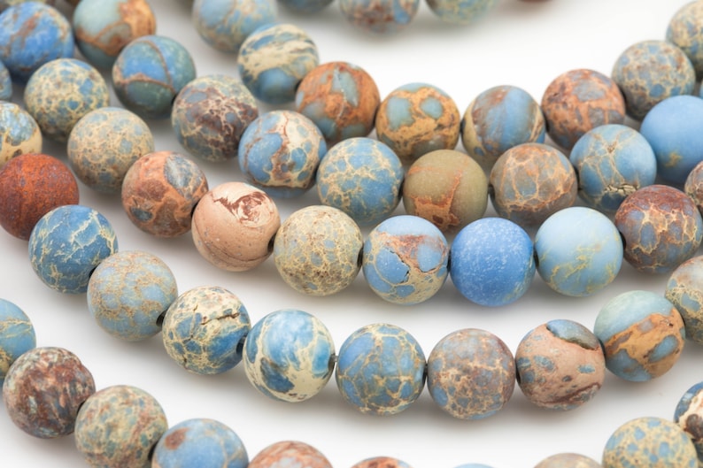 May include: A strand of blue, brown, and beige jasper beads. The beads are round and have a marbled pattern.