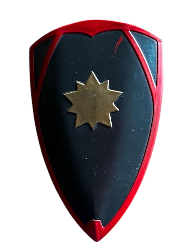 Pode incluir: Um escudo preto com borda vermelha e uma estrela dourada no centro.