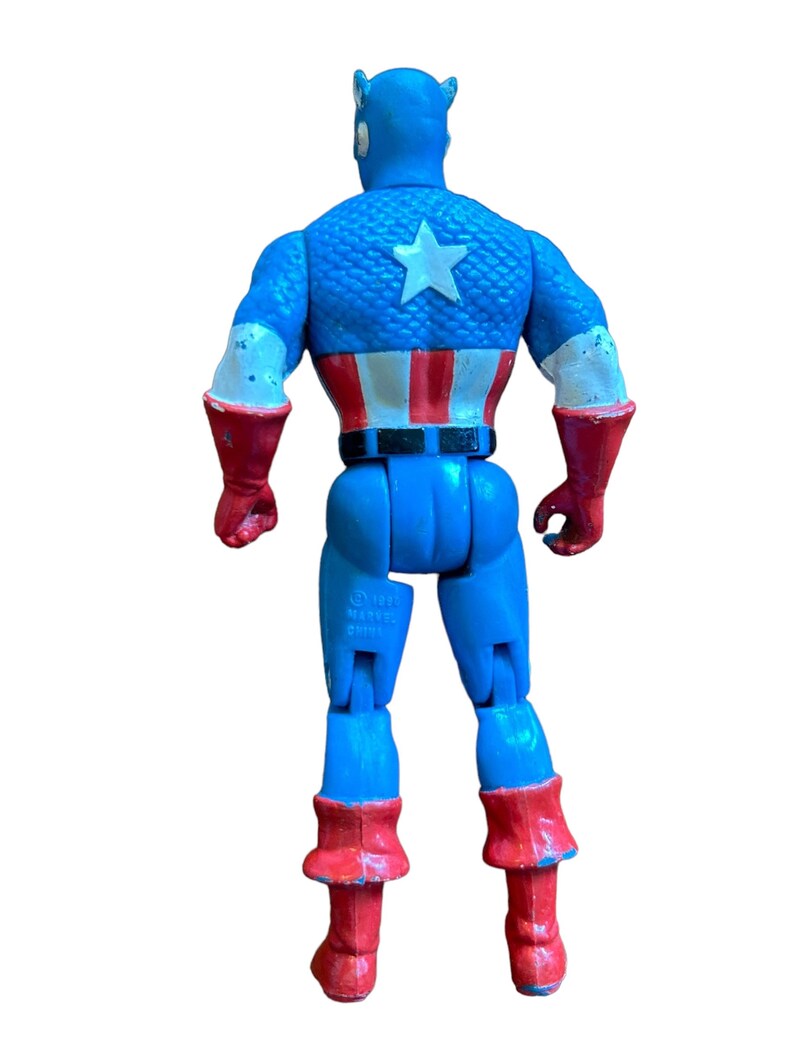 Puede incluir: Una figura de acci&oacute;n vintage de Capit&aacute;n Am&eacute;rica con un traje azul y rojo, una estrella blanca en el pecho y un cintur&oacute;n negro. La figura est&aacute; hecha de pl&aacute;stico y tiene brazos y piernas articulados. La figura est&aacute; de pie sobre un fondo blanco.