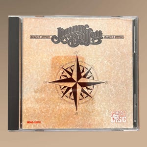 Pode incluir: Uma caixa de CD compacto com fundo bege e uma rosa dos ventos no centro. O texto "Jimmy Buffett" está impresso em preto na parte superior da caixa. O texto "Changes in Latitudes" está impresso em preto no lado esquerdo da caixa e o texto "Changes in Attitudes" está impresso em preto no lado direito da caixa. O texto "MCAD-31070" está impresso em vermelho na parte inferior esquerda da caixa. O texto "COMPACT DISC" está impresso em vermelho na parte inferior direita da caixa.