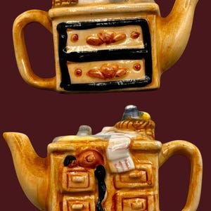 May include: A ceramic teapot shaped like a dresser with drawers. The teapot is brown and has a white handle. The teapot is decorated with a basket, a towel, and a hair dryer.