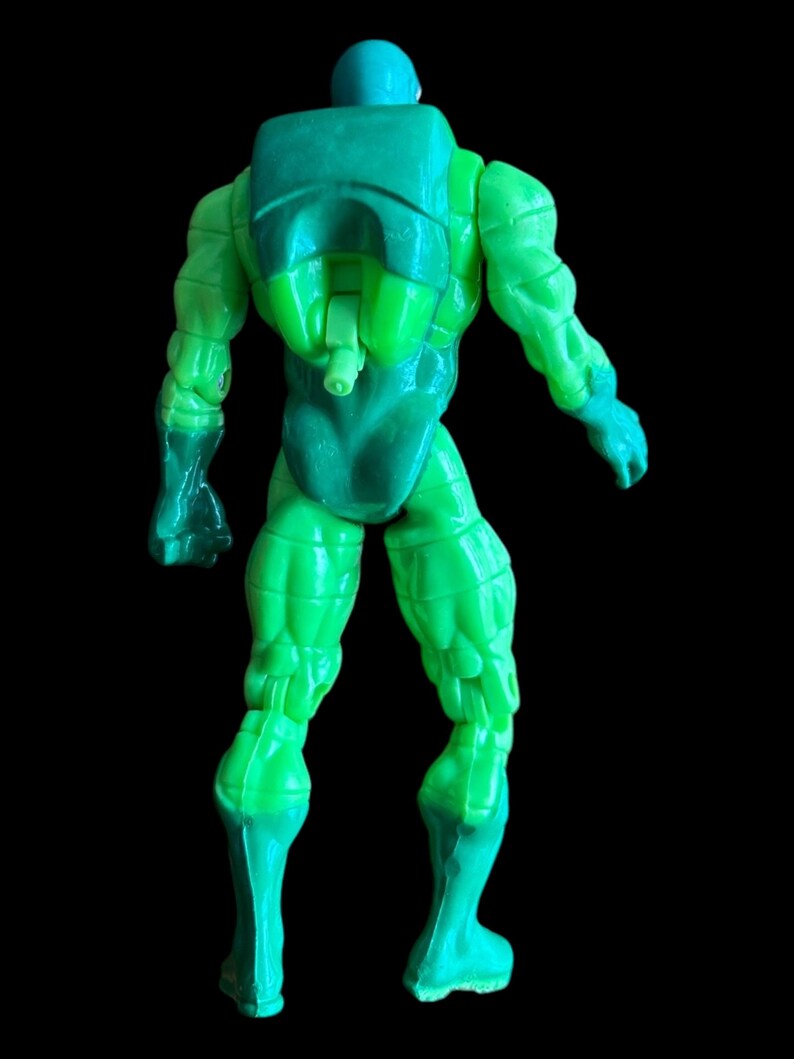 May include: A green action figure, seen from the back, with a backpack and helmet. The figure has a muscular physique and is posed with arms slightly extended. The legs are also visible, with a darker green shade at the feet.