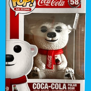 Może przedstawiać: Biała figurka winylowa polarnego niedźwiedzia Coca-Cola w czerwonym szaliku trzymająca butelkę Coca-Coli. Figurka znajduje się w przezroczystym plastikowym pudełku z czerwono-białym tłem. Pudełko ma logo Coca-Coli i napis "POP! AD ICONS". Numer 58 znajduje się w prawym górnym rogu pudełka.