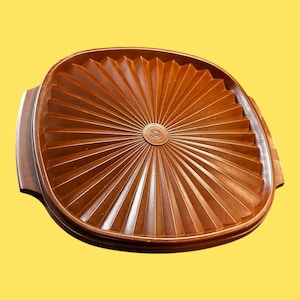 Puede incluir: Una tapa de plástico marrón con un diseño de rayos de sol. La tapa tiene un centro elevado con un patrón circular.