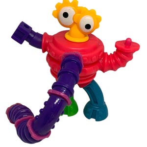 May include: A colorful plastic robot toy with a red body, purple and red arms, and teal and green legs. The robot has yellow gear-shaped eyes and a yellow neck. The toy is designed for children.