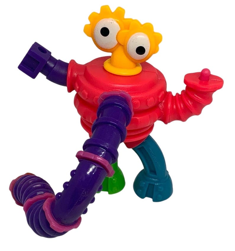 May include: A colorful plastic robot toy with a red body, purple and red arms, and teal and green legs. The robot has yellow gear-shaped eyes and a yellow neck. The toy is designed for children.