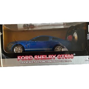 May include: A blue Ford Shelby GT500 radio-controlled car in its original packaging. The box displays the car's name and scale, 1:24. The car is blue with silver wheels. The packaging includes the Ford logo and the text "Full Function Radio Control."