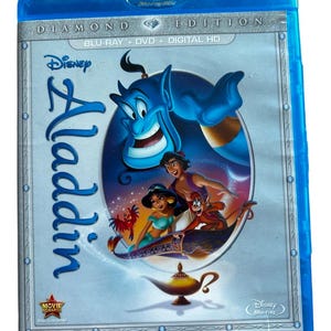 May include: A blue Blu-ray case with a silver border. The front of the case features a Disney logo and the title "Aladdin" in a silver font. The image on the case shows the characters Aladdin, Jasmine, and Abu riding on a magic carpet. The text "Diamond Edition" and "Blu-ray + DVD + Digital HD" are also visible on the case.