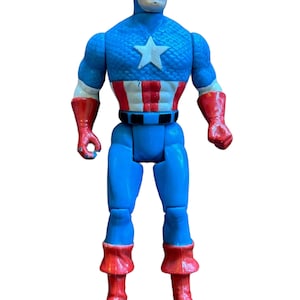 Puede incluir: Una figura de acci&oacute;n vintage de Capit&aacute;n Am&eacute;rica, con su ic&oacute;nico traje rojo, blanco y azul. La figura tiene un cuerpo azul, botas rojas y una estrella blanca en el pecho.