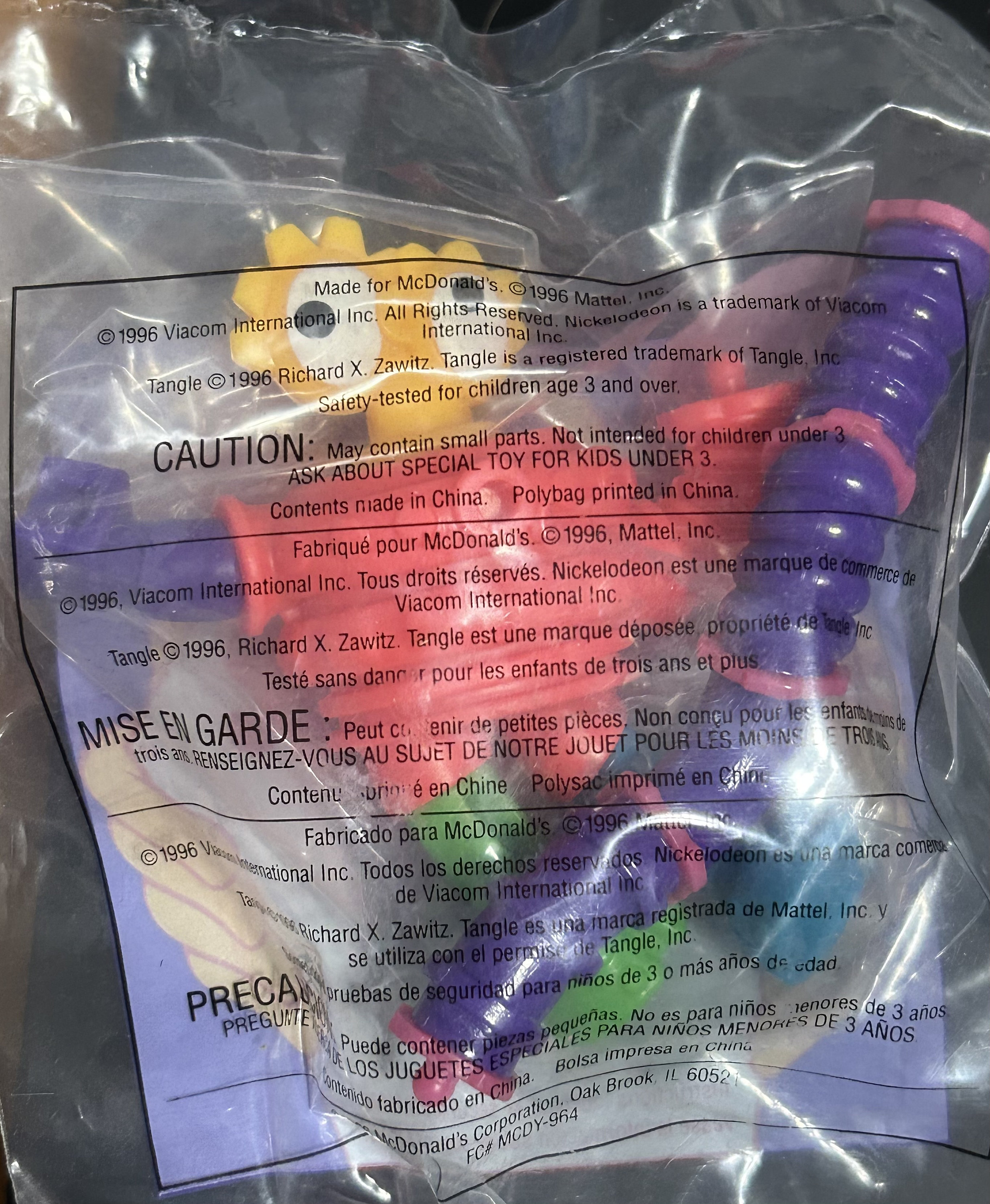May include: Sealed plastic bag containing a colorful toy. The toy appears to be a bendable, segmented figure with purple, red, yellow, and green sections. Text on the bag includes copyright information and a warning about small parts.