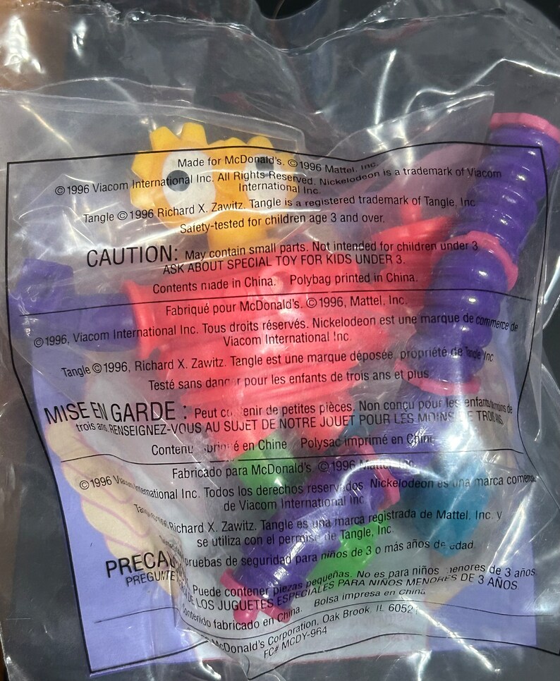 May include: Sealed plastic bag containing a colorful toy. The toy appears to be a bendable, segmented figure with purple, red, yellow, and green sections. Text on the bag includes copyright information and a warning about small parts.