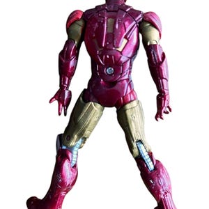 May include: A red and gold action figure of Iron Man, a superhero from the Marvel universe. The figure is posed with its arms outstretched and its legs slightly bent. The figure is made of plastic and has a detailed paint job.