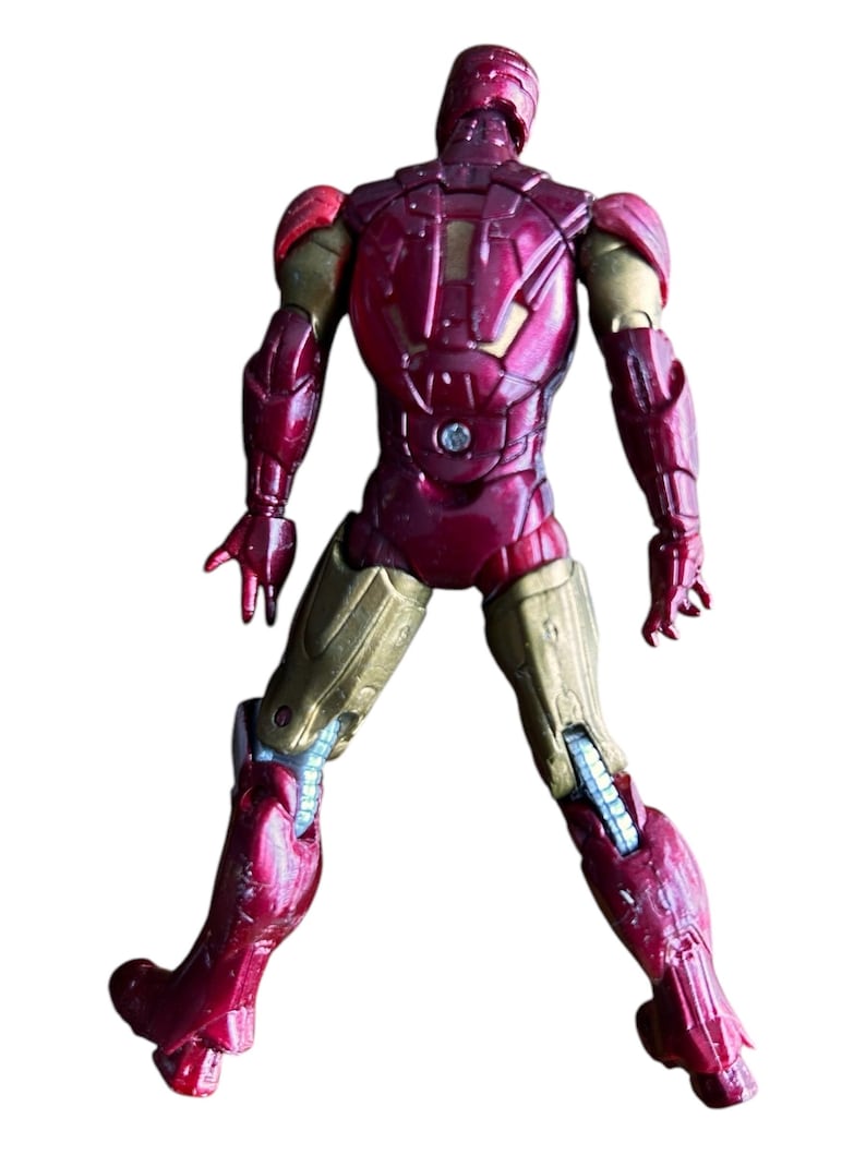 May include: A red and gold action figure of Iron Man, a superhero from the Marvel universe. The figure is posed with its arms outstretched and its legs slightly bent. The figure is made of plastic and has a detailed paint job.