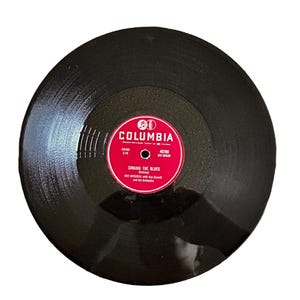 May include: A black vinyl record with a red label. The label has the Columbia Records logo and the text "Singing the Blues" by Guy Mitchell with Ray Conniff and his Orchestra.