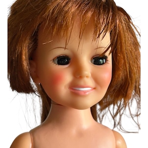 May include: A vintage doll with auburn hair and a smiling expression. The doll has rosy cheeks, black eyes, and a light skin tone. The doll's hair is styled with bangs and a side part. A classic toy.