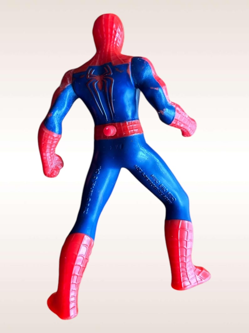 May include: A red and blue plastic action figure of Spiderman. The figure is posed with its arms outstretched and its legs spread apart. The figure has a red and blue suit with a spider logo on the chest. The figure is standing on a white background.