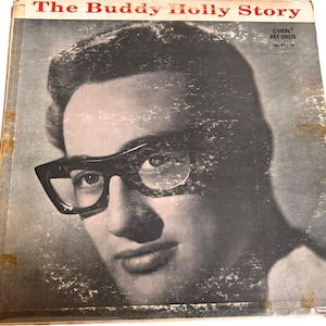 Puede incluir: Una foto en blanco y negro de Buddy Holly en la portada de un disco de vinilo. El disco se titula "The Buddy Holly Story" y es una publicación de Coral Records.
