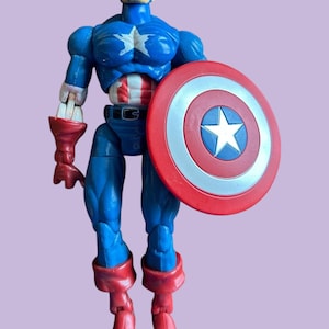 May include: A blue and red plastic action figure of Captain America holding his iconic red, white, and blue shield. The figure has a detailed face and a muscular build.