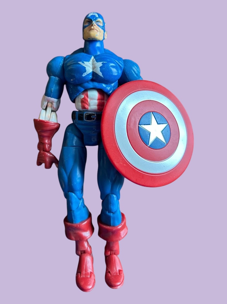 May include: A blue and red plastic action figure of Captain America holding his iconic red, white, and blue shield. The figure has a detailed face and a muscular build.