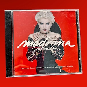 Może przedstawiać: Czerwona kaseta CD z fotografią Madonny na froncie. Tytuł albumu to "You Can Dance", a na dole kasety widnieje napis "Contains Three Special Dub Versions Available On CD Only".