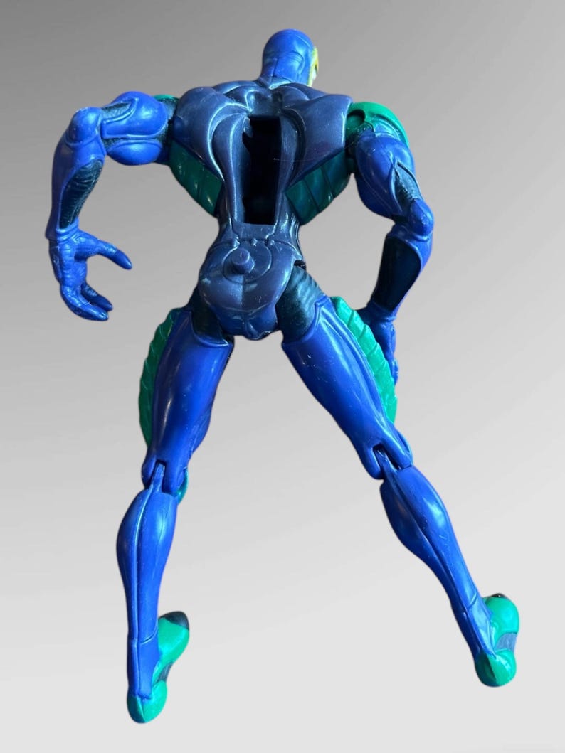 May include: Blue and green action figure with articulated limbs. The figure is posed with its back to the camera, arms bent at the elbows, and legs bent at the knees.
