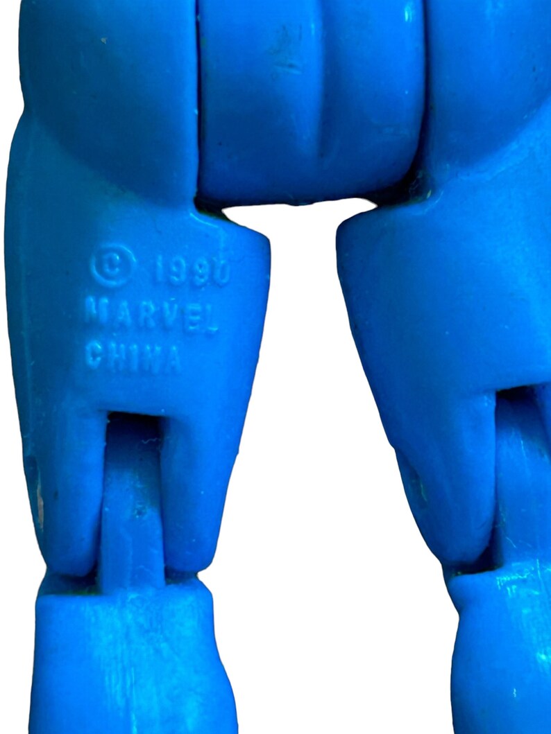 Puede incluir: Primer plano de las piernas inferiores de una figura de acci&oacute;n de pl&aacute;stico azul. Las piernas de la figura est&aacute;n dobladas por las rodillas. Los pies de la figura no son visibles. La figura tiene un s&iacute;mbolo de copyright y el texto "1990 MARVEL CHINA" impreso en la pierna izquierda.