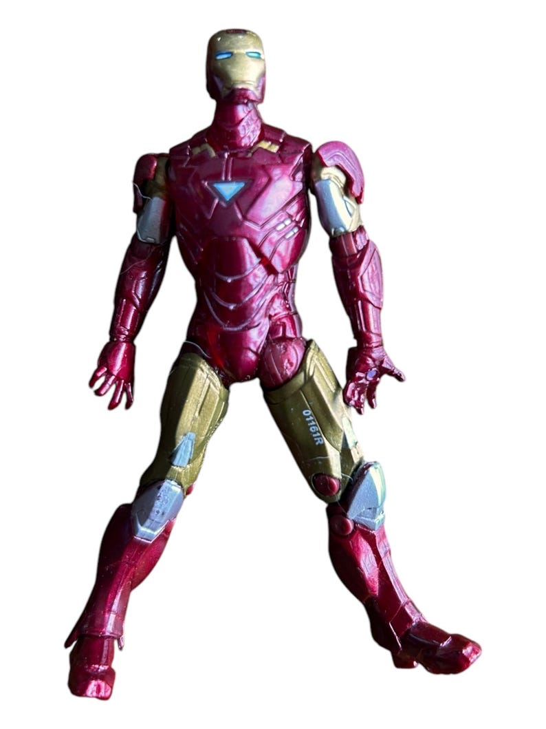 May include: Red and gold Iron Man action figure with a metallic finish. The figure is standing with its legs spread apart and its arms slightly raised. The figure has a blue and silver face mask and the text "0116IR" is printed on the right leg.