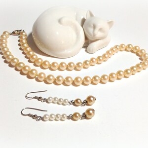 May include: A set of cream-colored pearl jewelry, including a necklace and earrings. The necklace is a single strand of pearls, and the earrings are simple pearl drops.