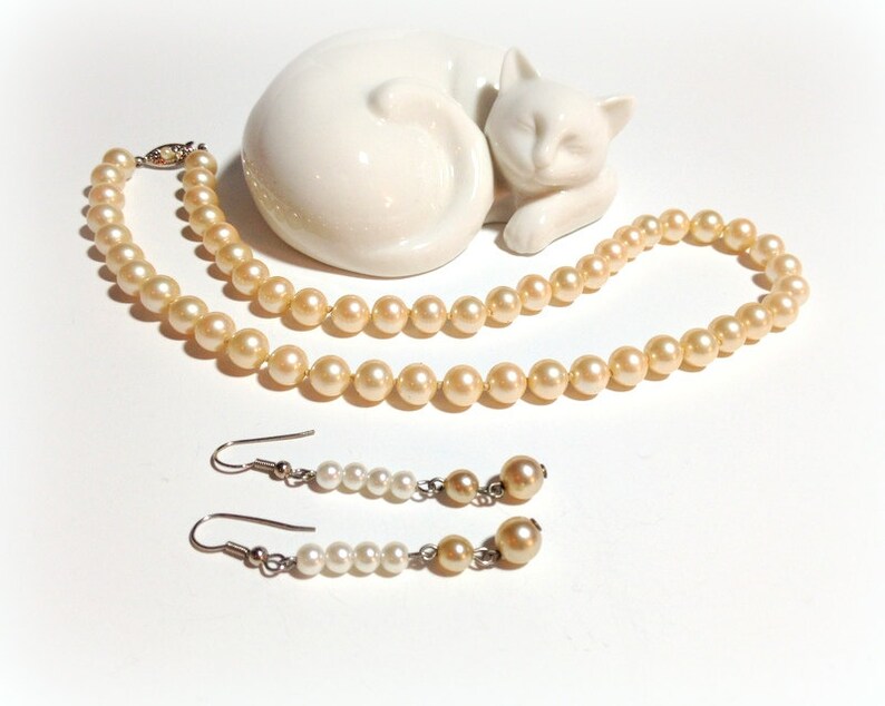 May include: A set of cream-colored pearl jewelry, including a necklace and earrings. The necklace is a single strand of pearls, and the earrings are simple pearl drops.