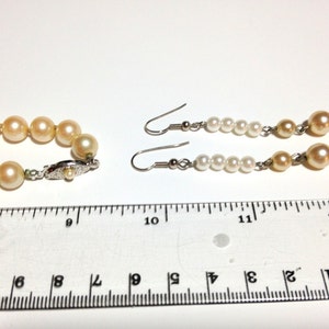May include: A pearl necklace and earrings set. The necklace is made of cream-colored pearls and has a silver clasp. The earrings are drop earrings with cream-colored pearls and silver hooks. The set is measured against a ruler.