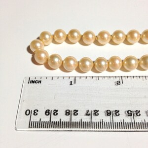 May include: A strand of cream-colored pearls with a ruler measuring 1 inch in length.
