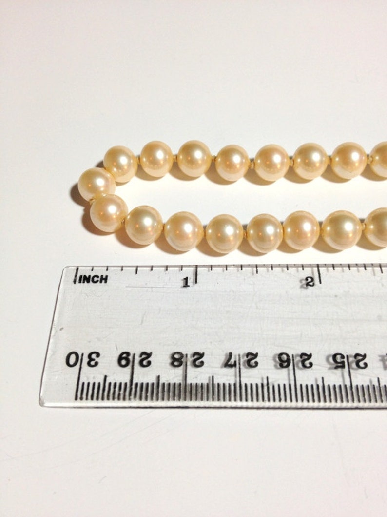May include: A strand of cream-colored pearls with a ruler measuring 1 inch in length.