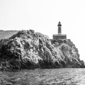 K&ouml;nnte beinhalten: Ein Schwarzwei&szlig;foto eines Leuchtturms auf einer felsigen Klippe mit Blick auf das Meer. Der Leuchtturm ist hoch und schlank, mit einem wei&szlig;en Turm und einem schwarzen Dach. Die Klippe ist rau und zerkl&uuml;ftet, mit ein paar B&auml;umen, die an ihren H&auml;ngen wachsen. Das Meer ist ruhig und still, mit ein paar Wellen, die an der K&uuml;ste brechen.