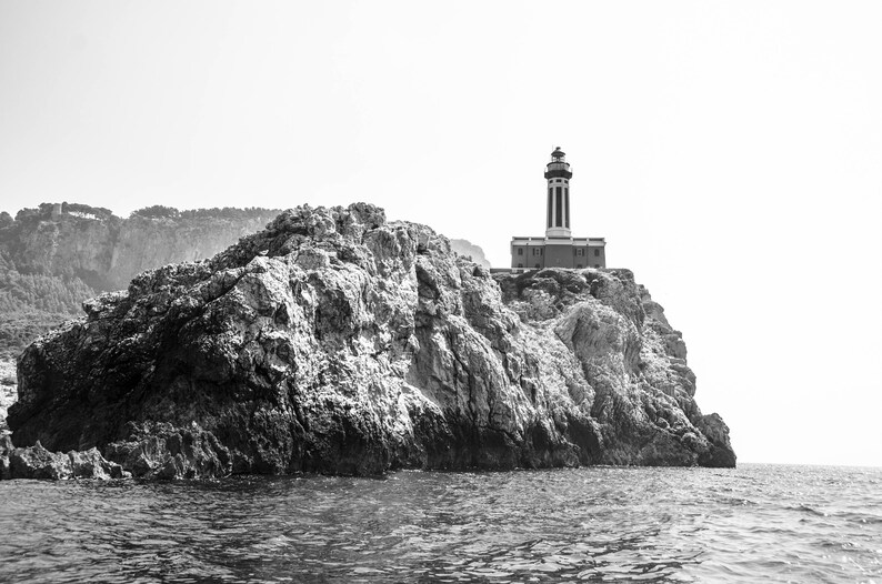 K&ouml;nnte beinhalten: Ein Schwarzwei&szlig;foto eines Leuchtturms auf einer felsigen Klippe mit Blick auf das Meer. Der Leuchtturm ist hoch und schlank, mit einem wei&szlig;en Turm und einem schwarzen Dach. Die Klippe ist rau und zerkl&uuml;ftet, mit ein paar B&auml;umen, die an ihren H&auml;ngen wachsen. Das Meer ist ruhig und still, mit ein paar Wellen, die an der K&uuml;ste brechen.