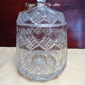 Puede incluir: Un tarro de cristal transparente vintage con tapa. El tarro tiene un patrón tallado en forma de diamante y un remate decorativo. El texto "Diggin Thru The Attic" es visible en la tapa. El tarro está sobre una superficie beige.
