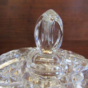 May include: A clear glass lid with a decorative knob on top. The lid has a cut glass pattern.