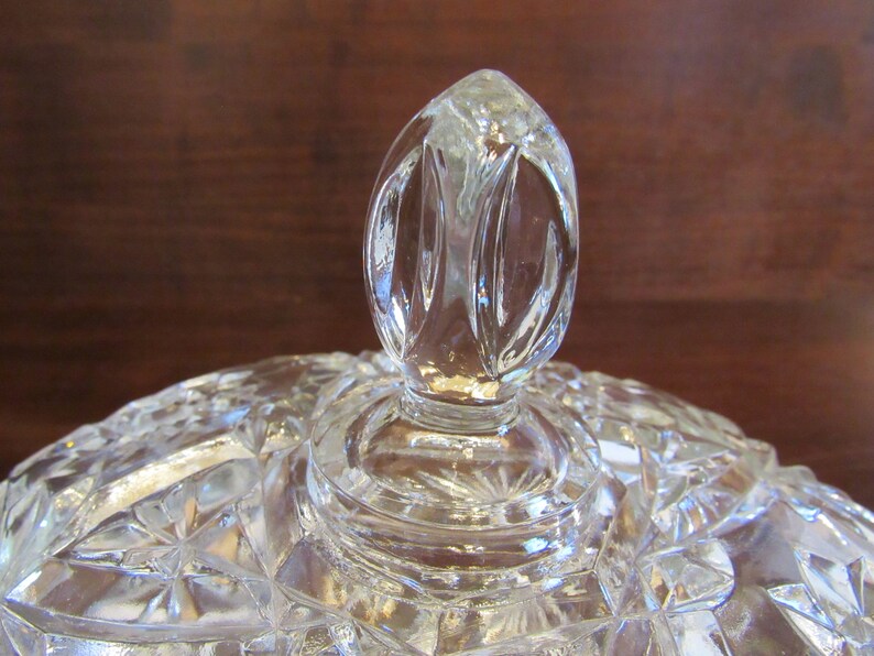 May include: A clear glass lid with a decorative knob on top. The lid has a cut glass pattern.