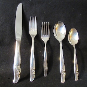 May include: A set of five silver-plated flatware pieces with floral designs on the handles. The set includes a knife, two forks, and two spoons.