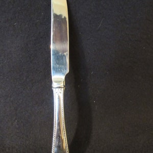 May include: A silver dinner knife with a detailed handle and a sharp blade.